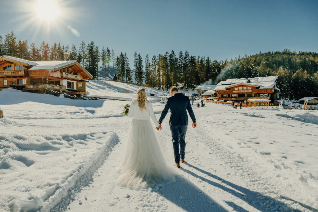 in lächelndes Brautpaar vor einer verschneiten Berghütte, bereit für ihre romantische freie Trauung